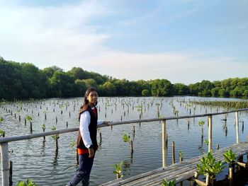 Full length portrait of woman standing by lake against sky