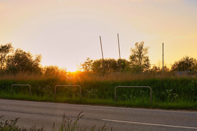 Street by field against sky during sunset