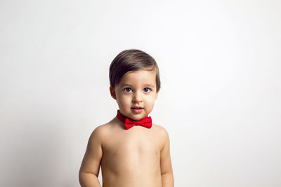 Child without a t-shirt sitting on a white background with a red bow tie