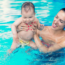 Close-up of mother holding cheerful shirtless toddler son in pool