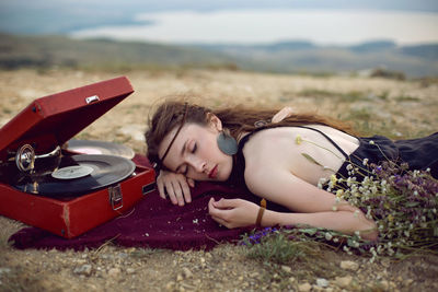 Young woman lies in nature in a black dress next to an old gramophone and listens to music