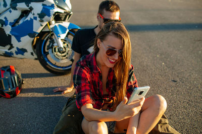 Young couple using mobile phone while sitting on road