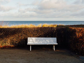 Empty bench on beach by sea against sky