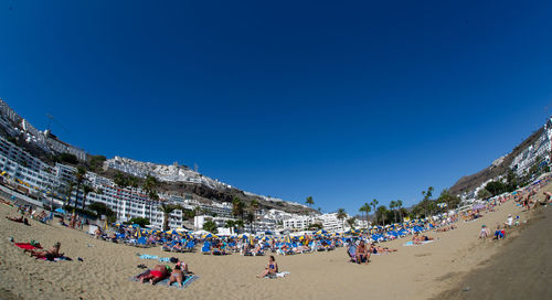 Group of people on beach against clear blue sky
