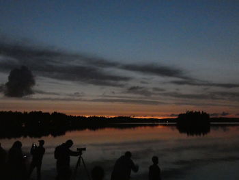 Silhouette people standing by trees against sky during sunset