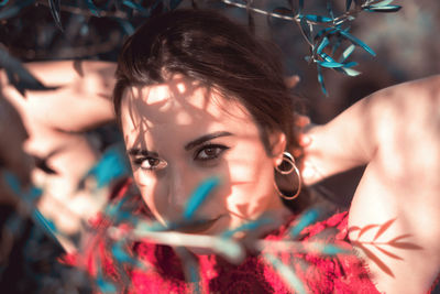 Close-up portrait of beautiful young woman looking through plant