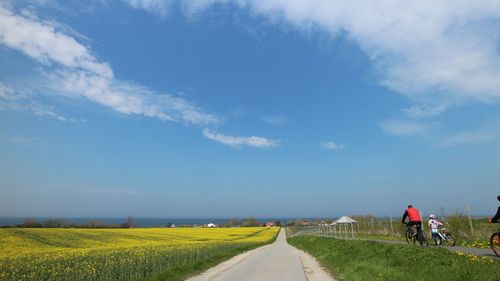 Road passing through field against sky