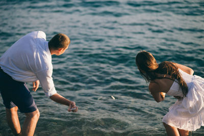 Rear view of couple skimming stones in lake