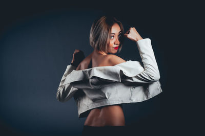 Rear view of seductive woman wearing jacket standing against black background