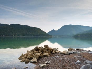 Big boulders sticking out from smooth lake water level. green blue water, mountain in water mirror.