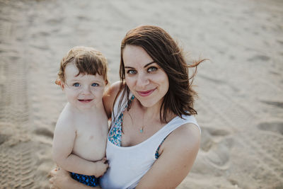 Smiling mother carrying son while standing at beach