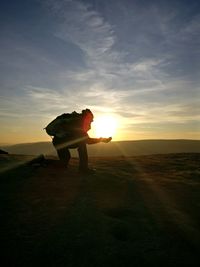 Side view of man standing on field against sky during sunset