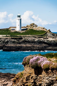 Lighthouse on cliff by sea against sky