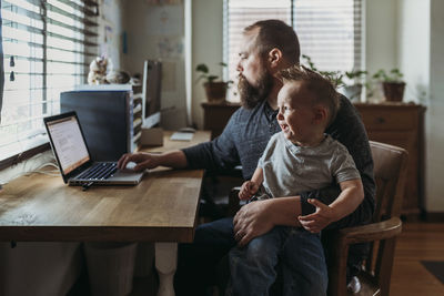 Dad working from home with one year old boy crying in his lap