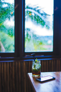 Drink in jar by window on table at home