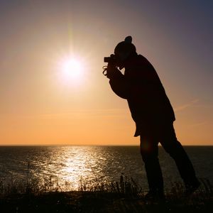Silhouette man photographing sea against sky during sunset