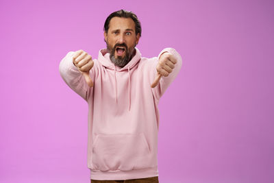 Displeased man showing thumbs down against purple background