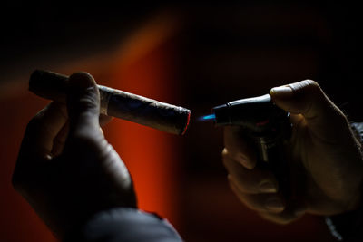 Cropped hand igniting cigar in darkroom