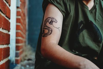Midsection of teenage boy with snake tattoo sitting outdoors