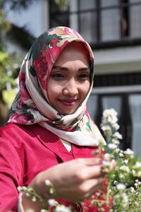 Smiling mid adult woman wearing hijab looking flowers in park