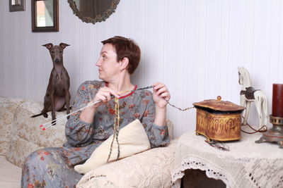 Woman weaving crochet while sitting on sofa at home