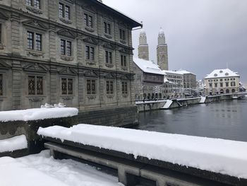 Snow covered buildings by canal against sky in city