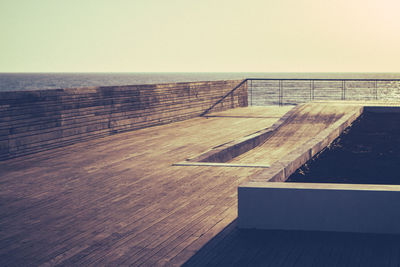 Wooden railing by sea against clear sky