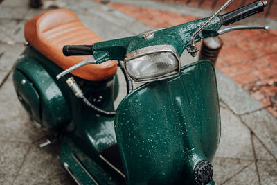 Classic green vespa scooter parked in the sidewalk.