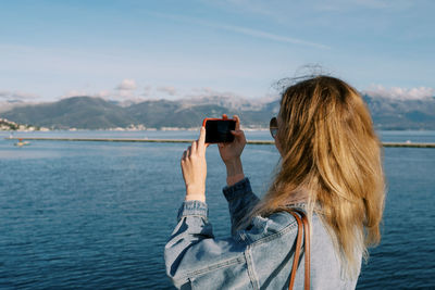 Side view of woman photographing sea against sky