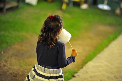 Rear view of girl eating cotton candy while walking at park