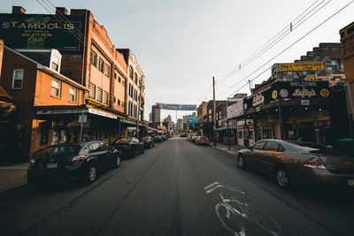 Cars on city street by buildings against sky