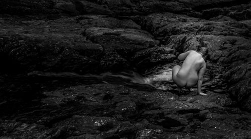 Rear view of naked woman crouching on rock