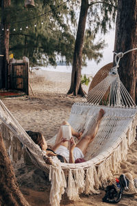Woman reading book while lying down in hammock on vacation at beach