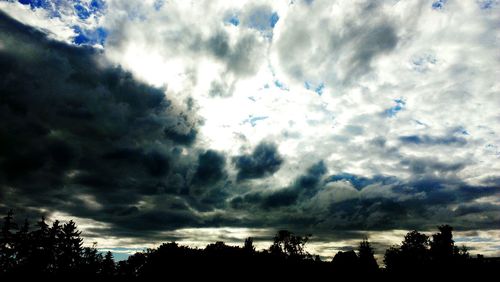 Low angle view of trees against cloudy sky