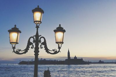 Street light by sea against sky during sunset