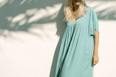 Woman standing in front of white wall on sunny day