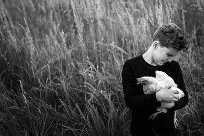 Full length of boy holding a hen on grass