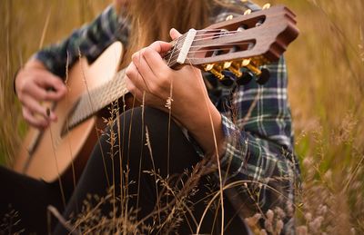 Midsection of woman playing guitar on field