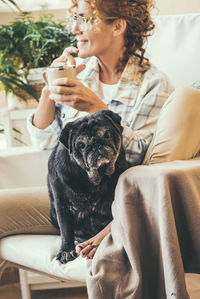 Smiling woman drinking coffee while sitting with dog