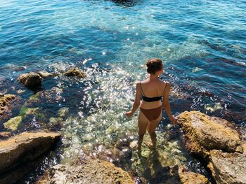 Rear view of woman standing in bikini on rocky shore