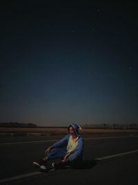 Man sitting on road against sky at night