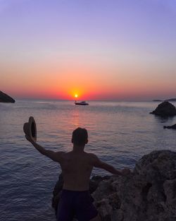 Man with hat standing at beach during sunset