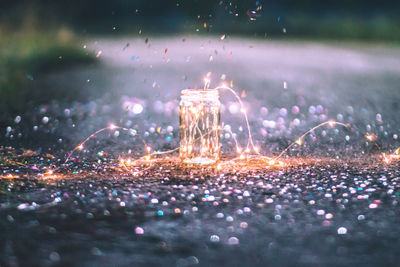 Confetti falling on illuminated string light in jar on road
