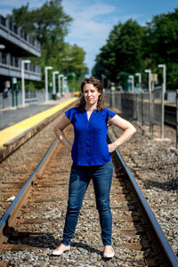 Portrait of woman with hands on hip while standing at railroad track