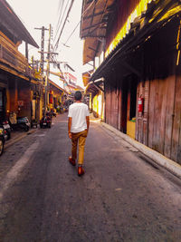 Rear view of man walking on street amidst buildings in city