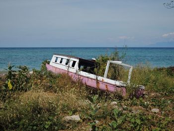Abandoned boat at sea shore against sky