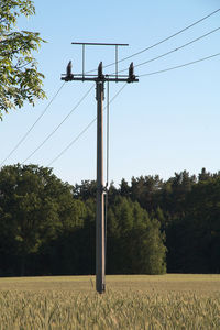 Low angle view of electricity pylon on field against clear sky