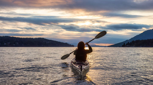 Rear view of woman standing in sea against sky during sunset