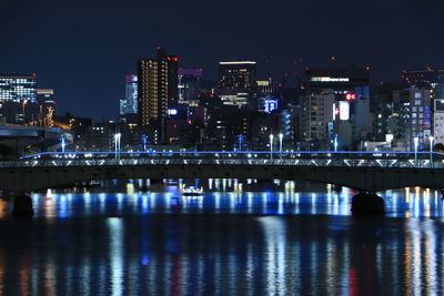 Illuminated modern buildings by river against sky at night