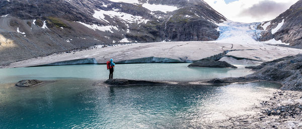 Full length of hiker standing on rock amidst glacial lake